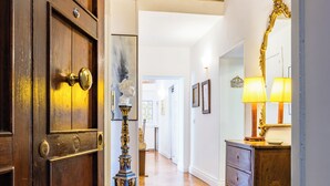 Un pasillo con suelo de madera, una puerta de madera con tirador de latón, una lámpara decorativa y un aparador con espejo.