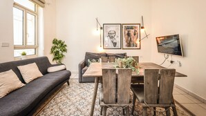 Ett modernt vardagsrum med en soffa, ett matbord, stolar, en tv och konstverk på väggen.