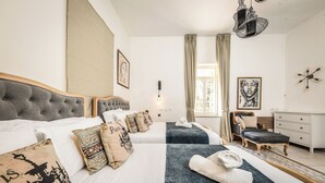 Ett hotellrum med två sängar, ett skrivbord, en stol och ett stort fönster med gardiner.