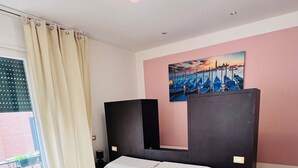A neatly made bed with white linens and towels, a painting of a cityscape on the wall, and a balcony with a view of the city. - L'affito Camera di Venezia (Mestre)
