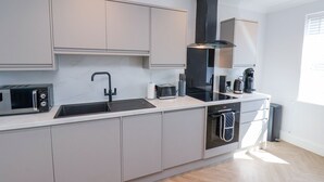 A modern kitchen with grey cabinets, a black sink, a built-in oven, a coffee maker, and a microwave. - The Salisbury - 1 Bedroom Deluxe Apartment (Scarborough)
