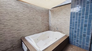 Un baño con pared de textura de piedra, una bañera y un revestimiento de azulejos azules.