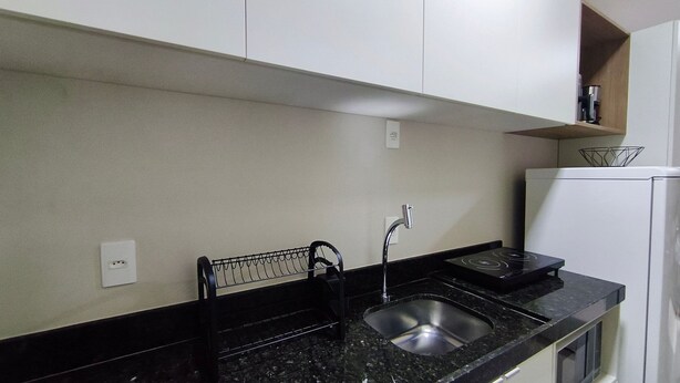 A kitchen with a black countertop, stainless steel sink, and a white refrigerator. - Ora Beach (Ipojuca)