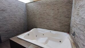 A bathroom with a stone-textured wall, a white bathtub, and a wooden bench. - Ora Beach (Ipojuca)