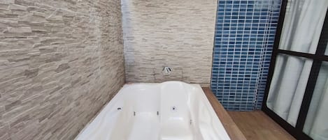 Un baño moderno con pared de piedra, zona de ducha con azulejos azules y una bañera grande.