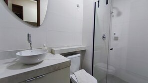 A modern bathroom with a vessel sink, a mirror, a toilet, and a glass shower enclosure. - Ora Beach (Ipojuca)