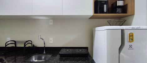 A kitchen with a sink, stove, and a white refrigerator with a can magnet.
