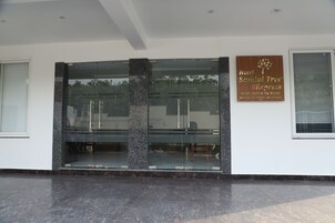 A modern hotel entrance with a glass facade, a signboard for 'Hotel Sandal Tree Express' and a reception desk.
