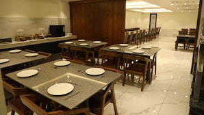 A dining area with multiple tables set for meals, equipped with plates, cutlery, and glasses. - Hotel Sandal Tree Express (Noida)