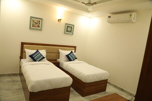 A hotel room with two single beds, a ceiling fan, wall-mounted air conditioning, and two framed pictures on the wall.