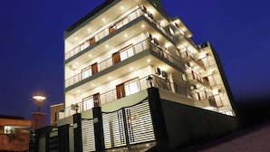 A multi-story building with balconies, a gated entrance, and a well-lit facade. - Hotel Sandal Tree Express (Noida)