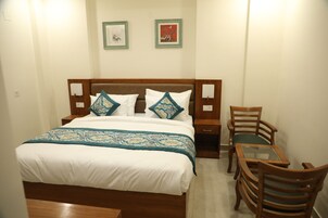 Ein ordentlich eingerichtetes Schlafzimmer mit einem Bett, Nachttischen, einem Sessel und einem kleinen Tisch.