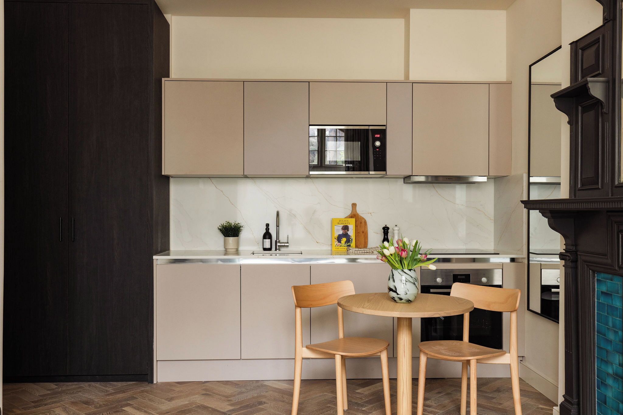 Una cocina moderna con armarios de madera oscura, un microondas integrado y una mesa redonda de madera con dos sillas.