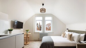 A bedroom with a bed, a TV, a window, a radiator, and a small table with a plant. - FiveM West Hampstead - South (London)