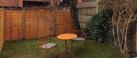 A backyard with a wooden fence, two metal chairs, and a small round table.