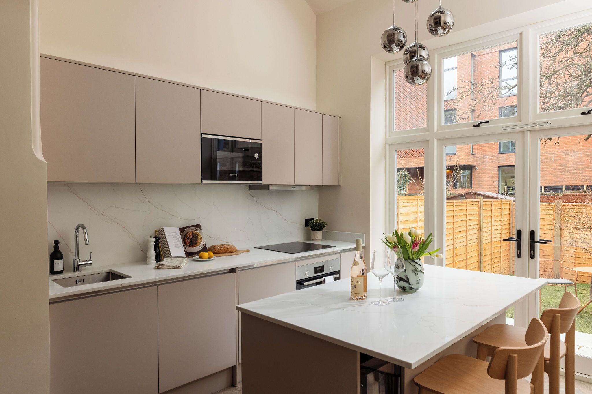Een moderne keuken met een centraal eiland, een ingebouwde oven en een groot raam met uitzicht op een tuin.