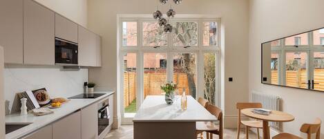 Una cocina moderna con una isla central, una zona de comedor con sillas de madera y grandes ventanales que ofrecen vistas al exterior.