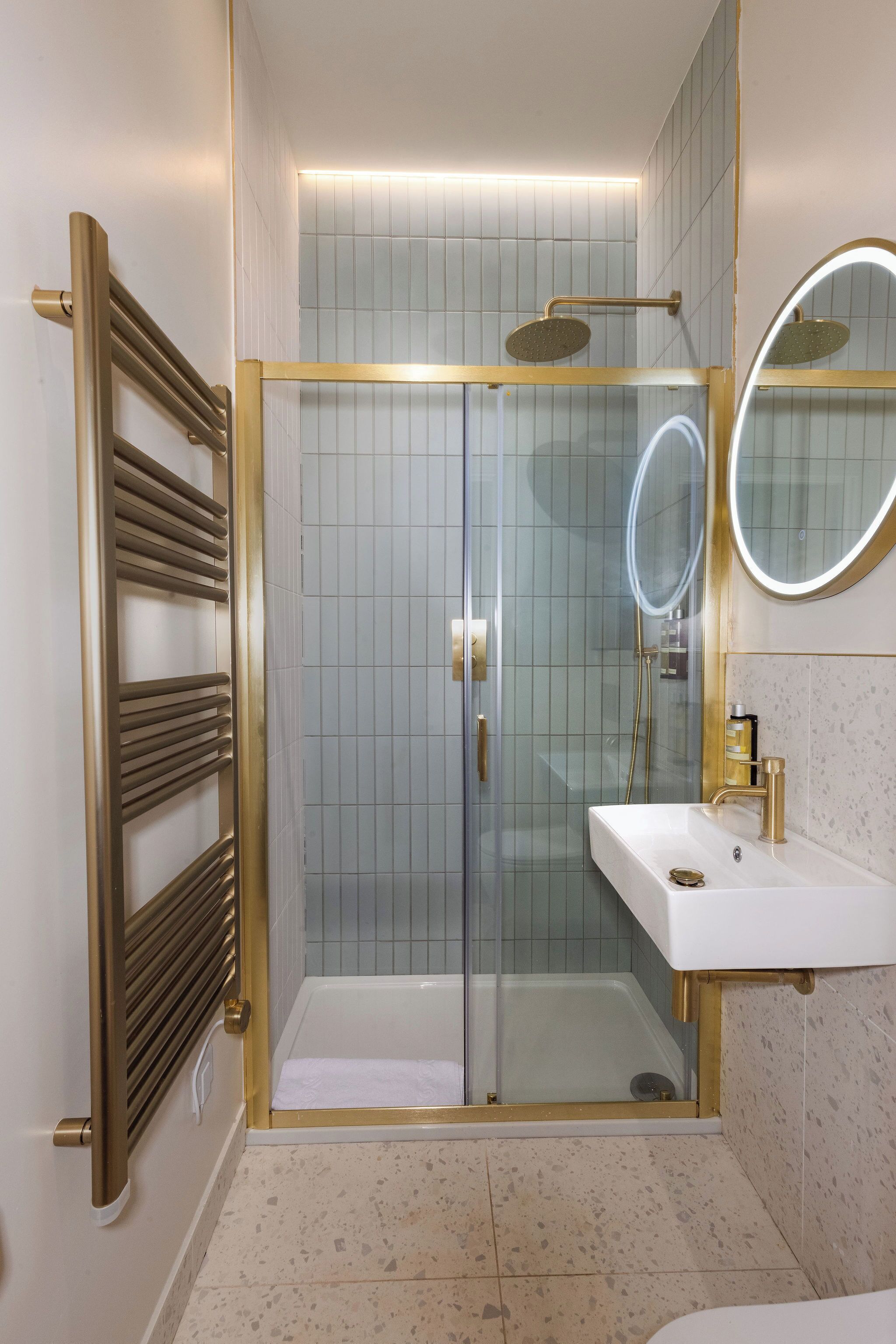 A modern bathroom with a glass-enclosed shower, a white sink with gold fixtures, and a large mirror.