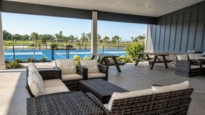 An outdoor patio area with wicker furniture, a pool, and a view of the tennis court.