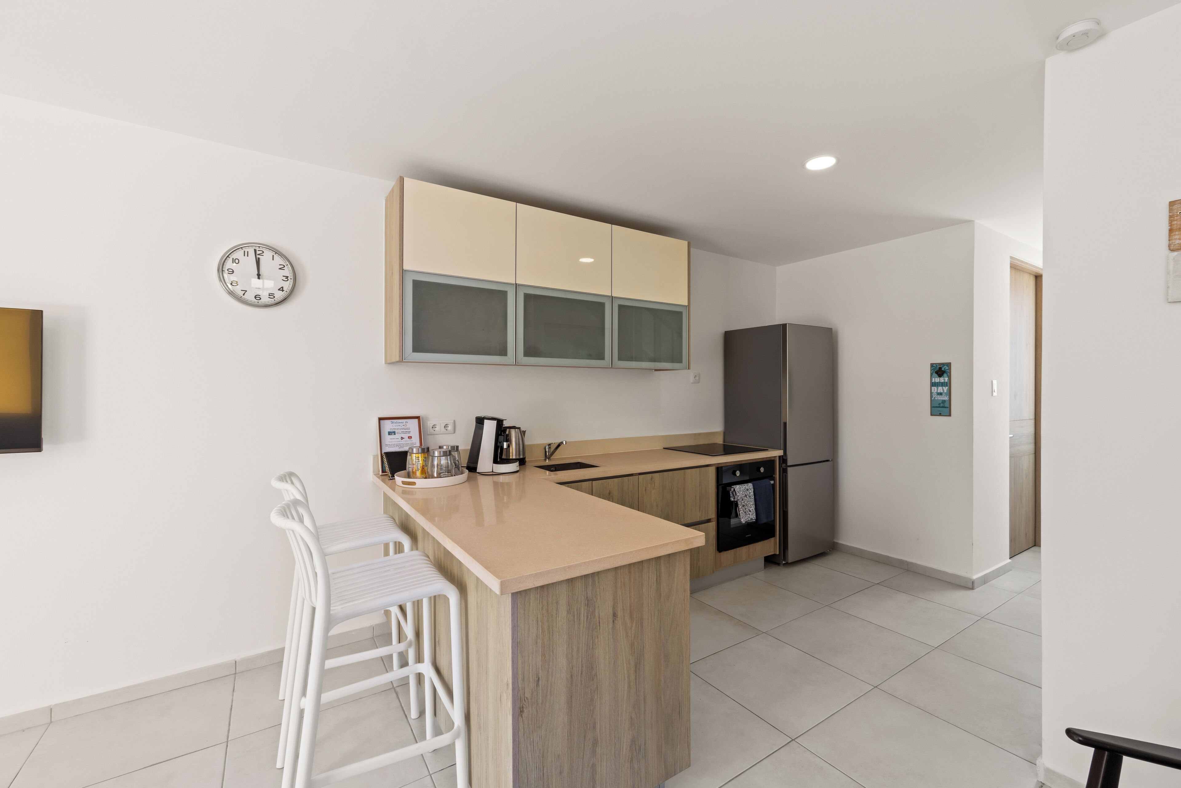 Une cuisine moderne avec un îlot central, des tabourets de bar, un réfrigérateur et une horloge au mur.