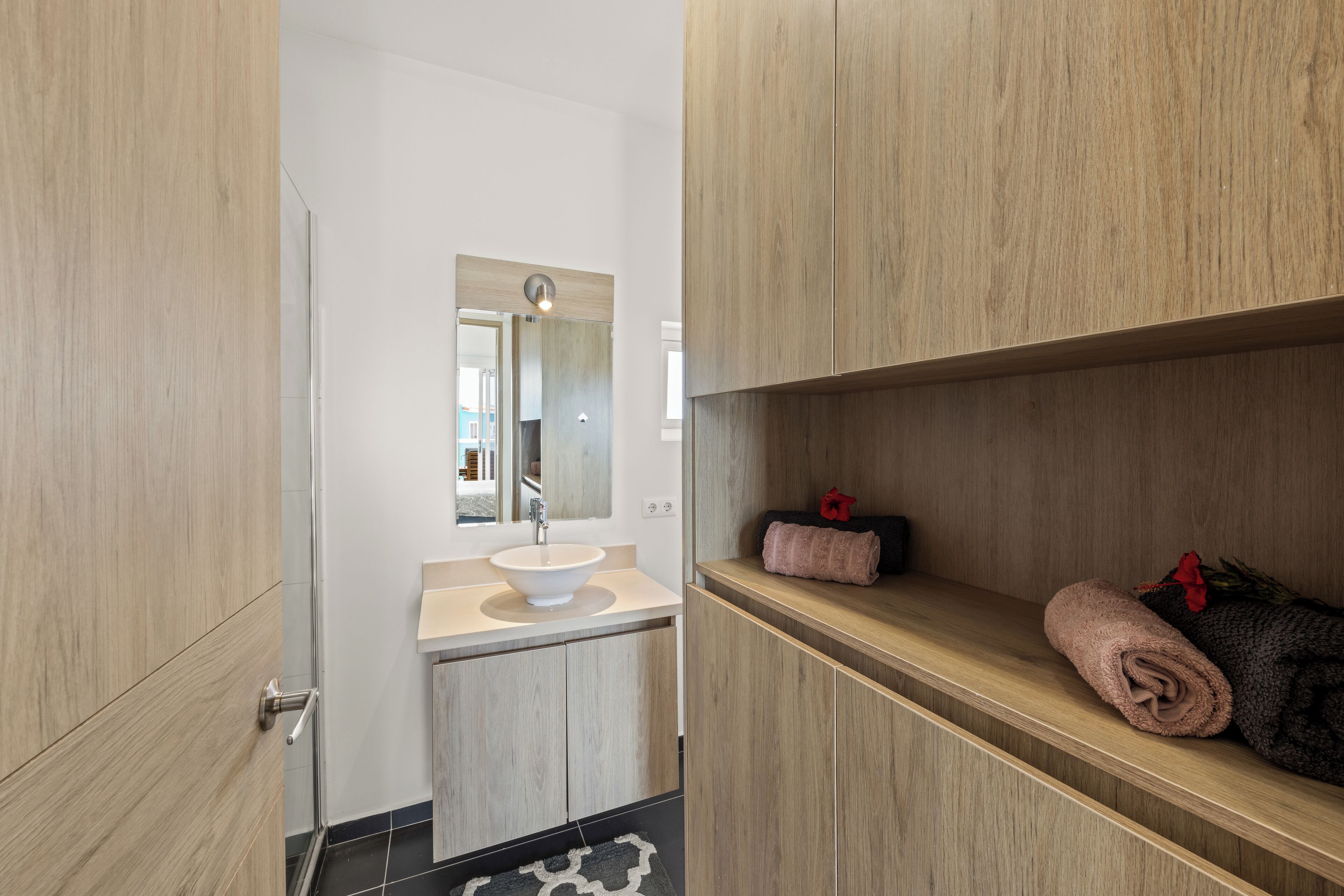 Un baño moderno con muebles de madera, un lavamanos blanco y un espejo encima.
