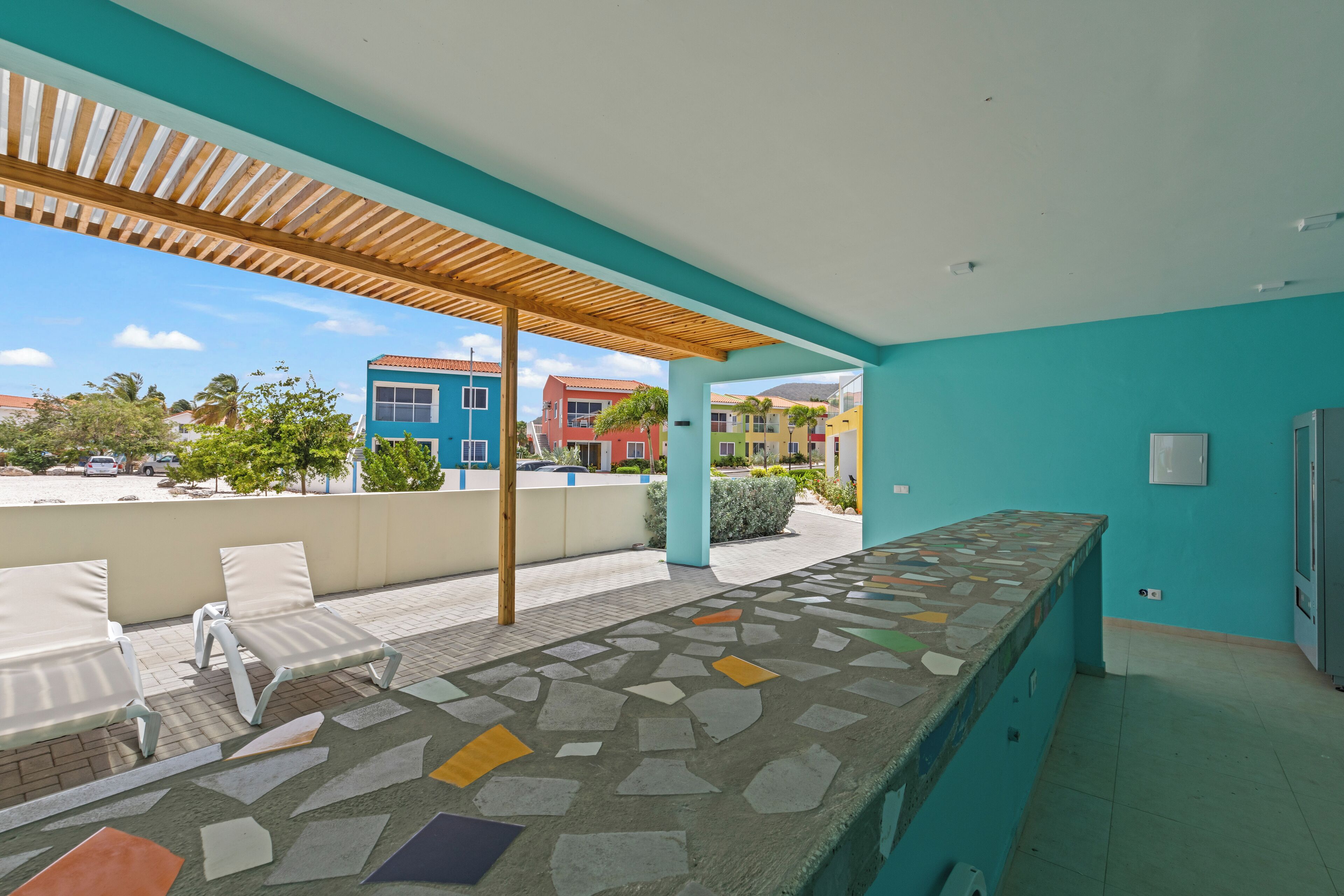 A covered outdoor area with a stone-tiled counter and lounge chairs.