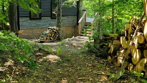 Une cabane rustique avec des fondations en pierre, une terrasse en bois et une pile de bois de chauffage.