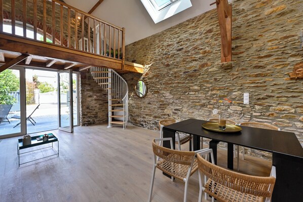 A spacious room with a stone wall, a wooden staircase, a dining table with chairs, and a glass coffee table.