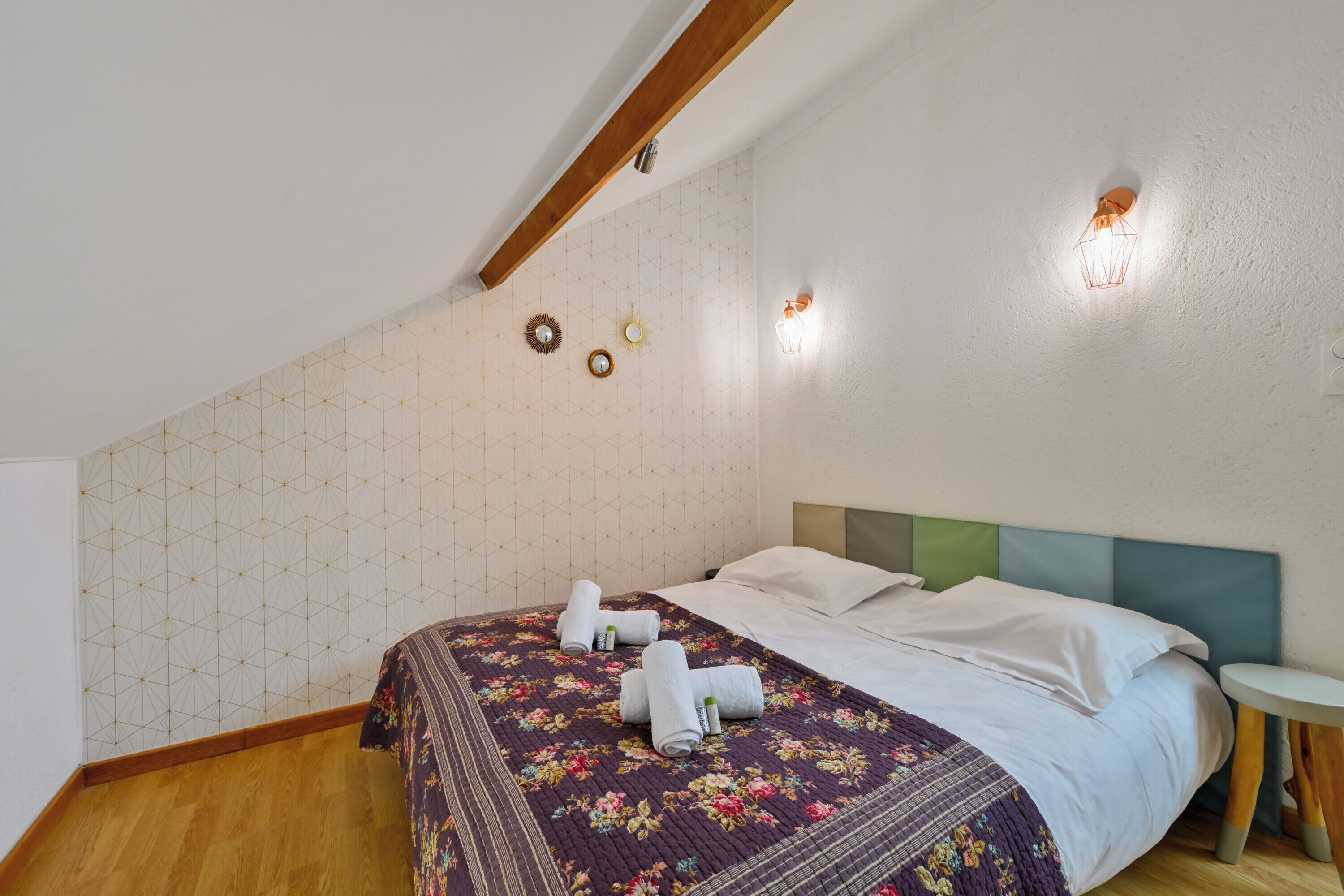 Une chambre avec un plafond en bois, une couvre-lit à motifs floraux et deux appliques murales.