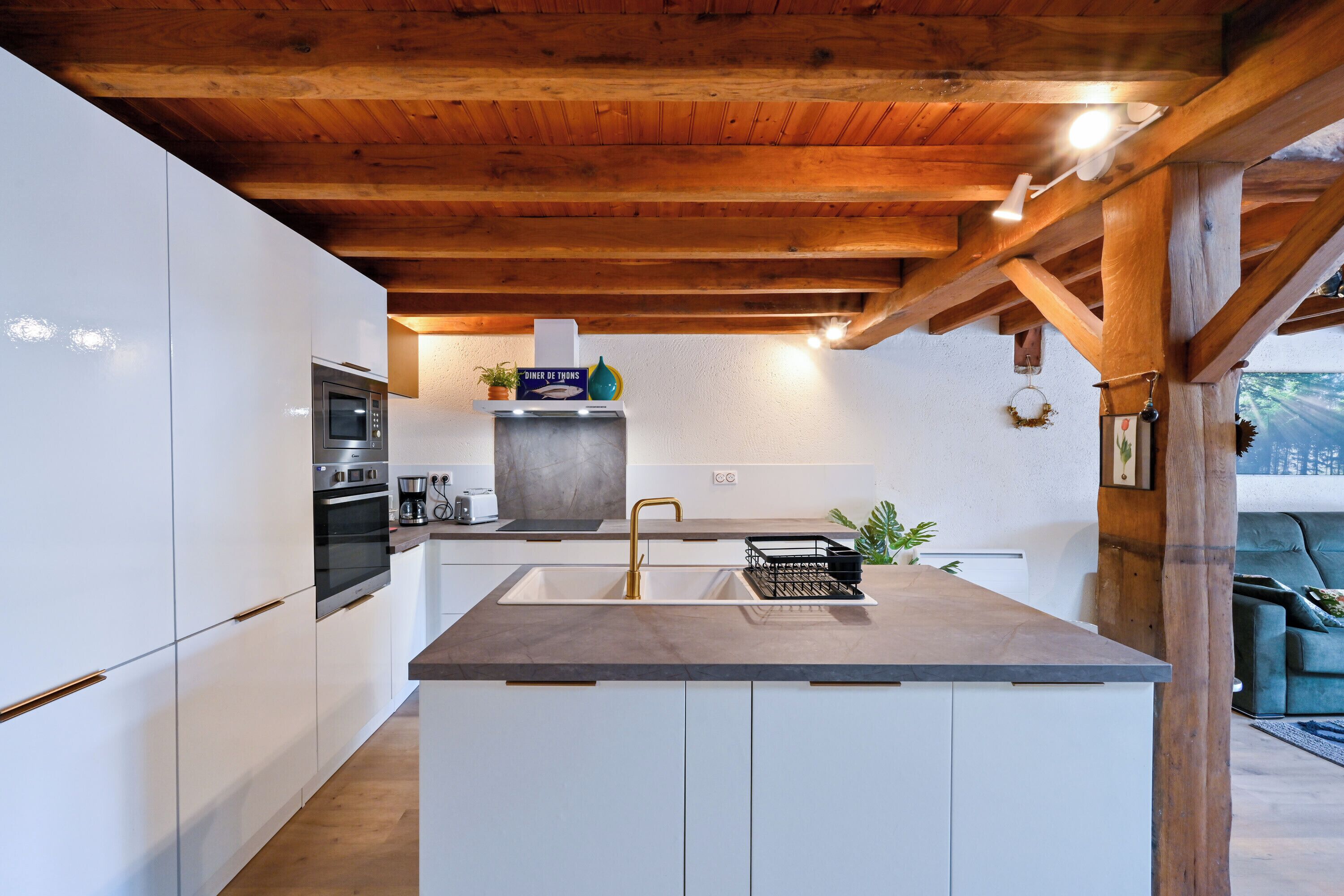 Eine moderne Küche mit weißen Schränken, einer zentralen Kochinsel mit Spüle und Holzbalken an der Decke.