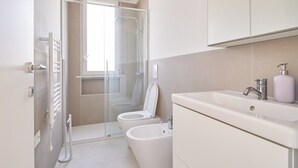Un baño moderno con cabina de ducha de vidrio, inodoro, bidé y lavamanos con espejo superior.