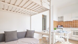 Una habitación moderna y luminosa con sofá, una pequeña mesa de comedor y una zona de cocina.