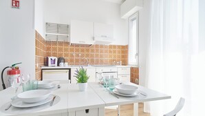 Una cocina moderna con armarios blancos, salpicadero de azulejos y un comedor con una mesa blanca dispuesta para dos personas.