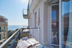 Een balkon met uitzicht op zee, een tafel met een tijdschrift en een stoel.