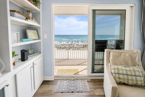 Ein Zimmer mit Blick auf den Strand, eine Sitzecke, ein Bücherregal und eine Glastür zum Balkon.