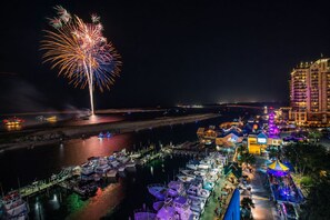 A marina with boats docked, a waterfront building, and fireworks in the sky. - Beachfront Bliss! Gulf Waves at The Palms #201 (Okaloosa Island)