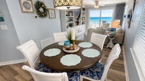 Een eetruimte met een ronde tafel, witte stoelen en uitzicht op de oceaan door grote ramen.
