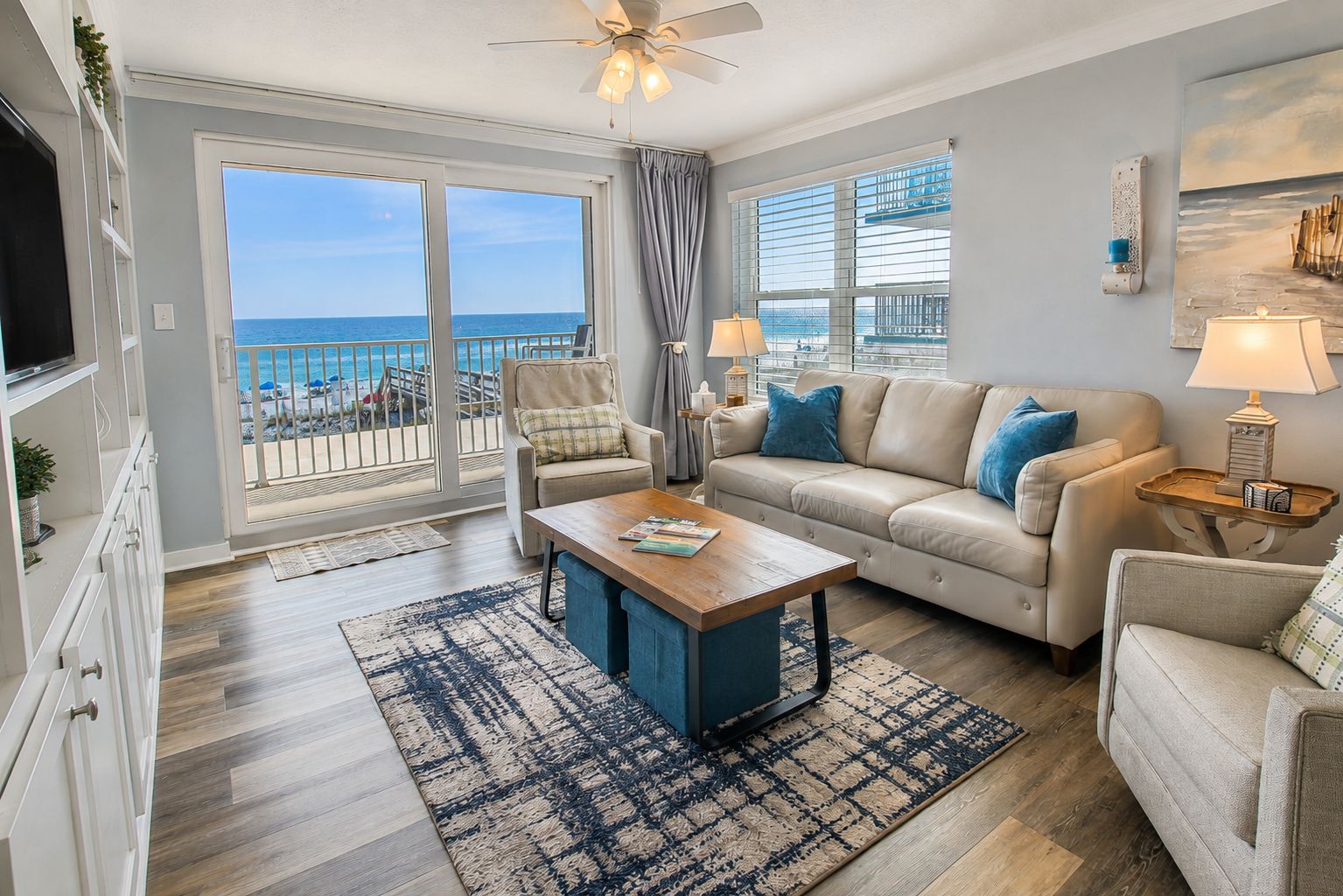 A living room with a sofa, armchairs, a coffee table, and a TV. There is a balcony with a view of the ocean.
