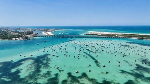 An aerial view of a coastal area with a large number of boats on the water, a bridge, and a cityscape in the background. - Beachfront Bliss! Gulf Waves at The Palms #201 (Okaloosa Island)