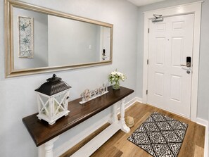 Un couloir avec une console en bois foncé, une porte blanche, un grand miroir et un tapis à motifs.
