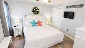 Een slaapkamer met een bed, nachtkastjes, een plafondventilator, een televisie en een muur met een bordje waarop staat 'choose happiness'.