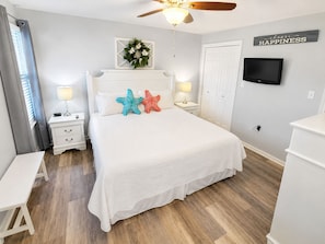 A bedroom with a bed, bedside tables, a ceiling fan, a TV, and a wall with a 'choose happiness' sign. - Beachfront Bliss! Gulf Waves at The Palms #201 (Okaloosa Island)