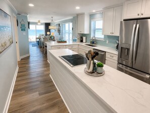 A modern kitchen with white cabinetry, a stainless steel refrigerator, and a central island with a built-in stove. - Beachfront Bliss! Gulf Waves at The Palms #201 (Okaloosa Island)