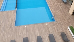 A rooftop pool area with a rectangular pool, lounge chairs, and a dining area with tables and chairs. - PREMIUM SUITE (Accra)