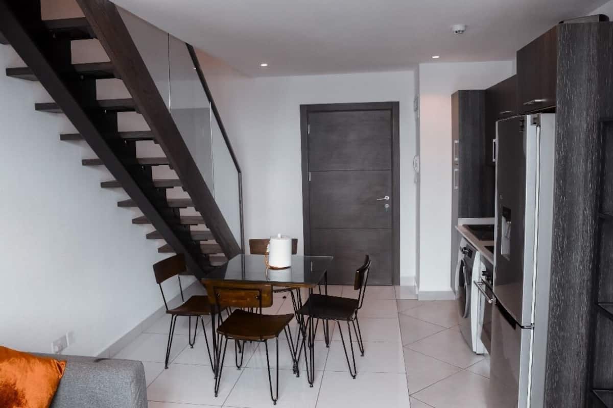 A modern kitchen with a built-in refrigerator, a dining area with a table and chairs, and a staircase leading to an upper level.
