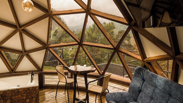 Una habitación tipo cúpula geométrica con suelo de madera, una mesa redonda, dos sillas, un sofá y una bañera junto a la pared.