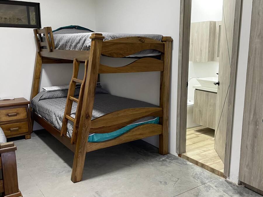 A bunk bed with a desk and drawers, a bathroom with a sink and mirror, and a door leading to another room.