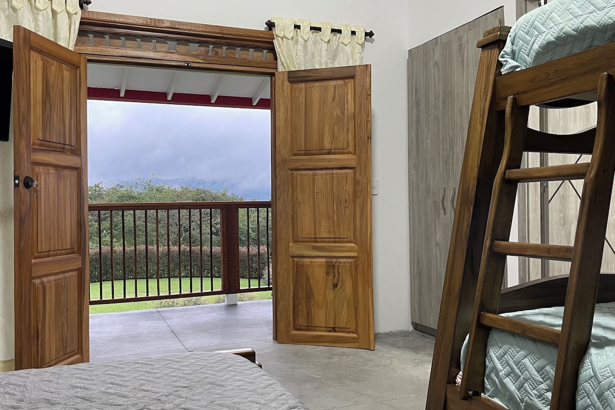 A bedroom with a wooden door leading to a balcony, a bunk bed, and a TV mounted on the wall.