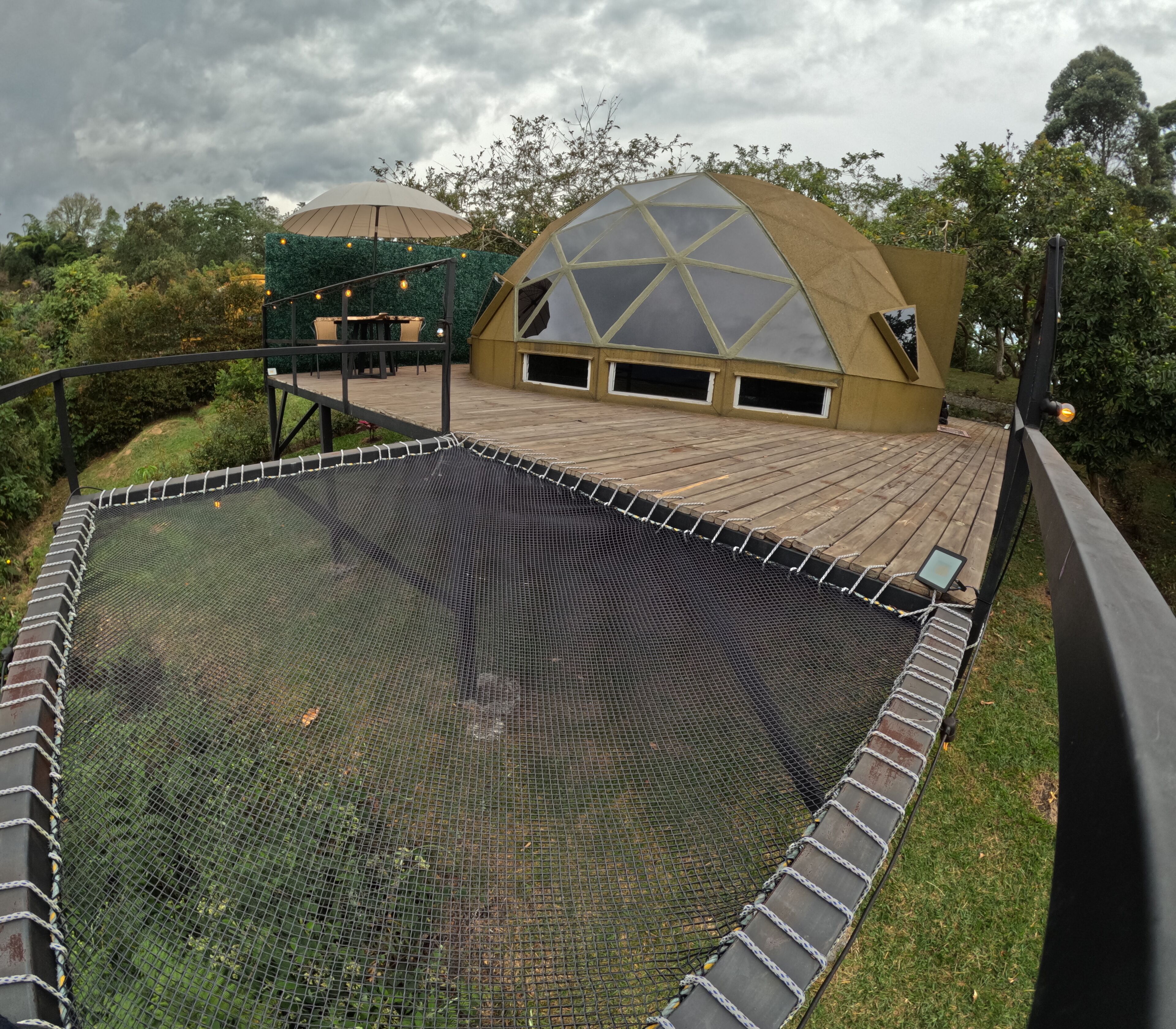 Un toit-terrasse doté d’un espace de jeux protégé par un filet, d’une terrasse en bois et d’un bâtiment en forme de dôme avec des fenêtres.