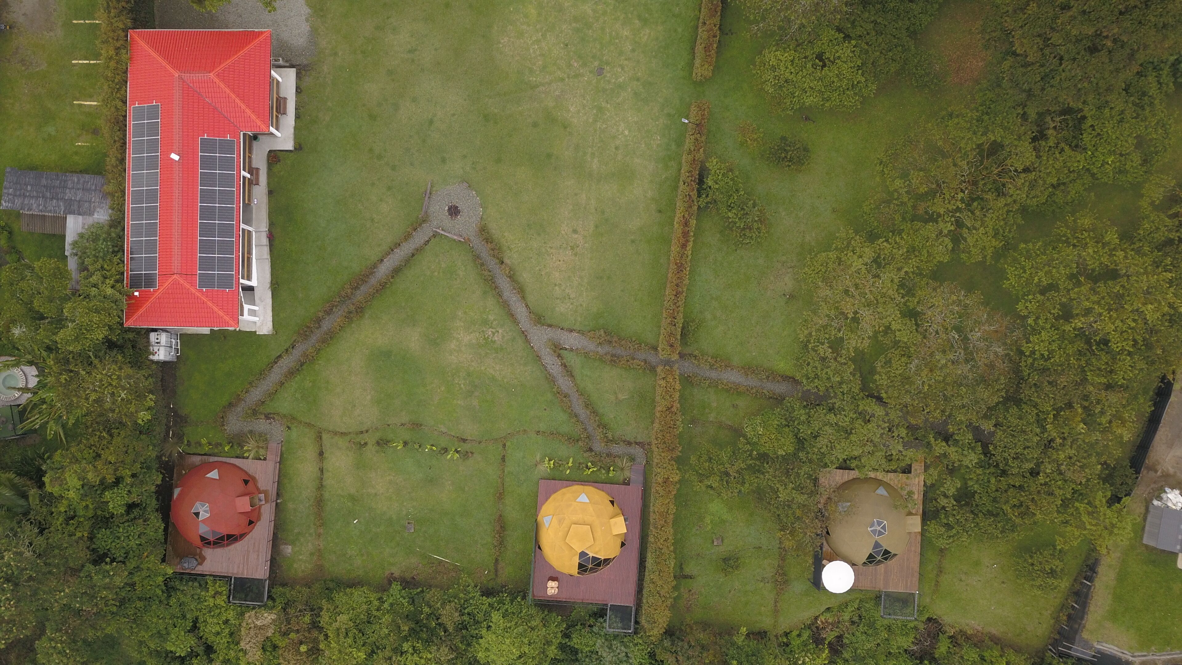 An aerial view of a property with a large building with a red roof, three distinct structures with unique roof designs, and a central pathway.